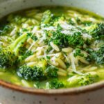 Broccoli orzo soup with grated Parmesan and fresh herbs in a ceramic bowl