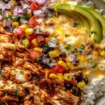 High protein chicken enchilada bowl with shredded chicken, rice, black beans, corn, melted cheese and avocado