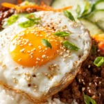 Korean ground beef bowl with jasmine rice, fried egg, sesame seeds, cucumbers, and carrots